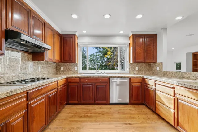 a kitchen with stainless steel appliances granite countertop wooden cabinets a sink and dishwasher a oven with wooden floors
