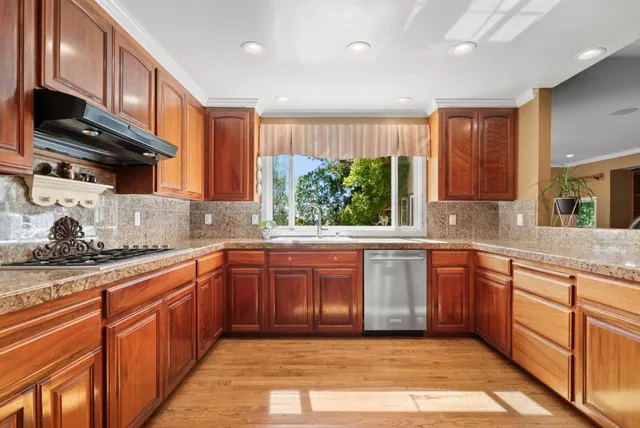 a kitchen with stainless steel appliances granite countertop wooden cabinets a stove a sink and a large window