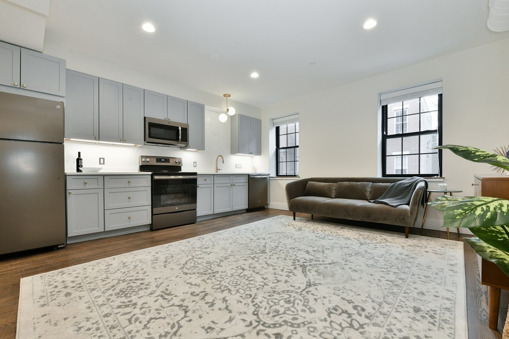 a living room with stainless steel appliances furniture a rug and a window