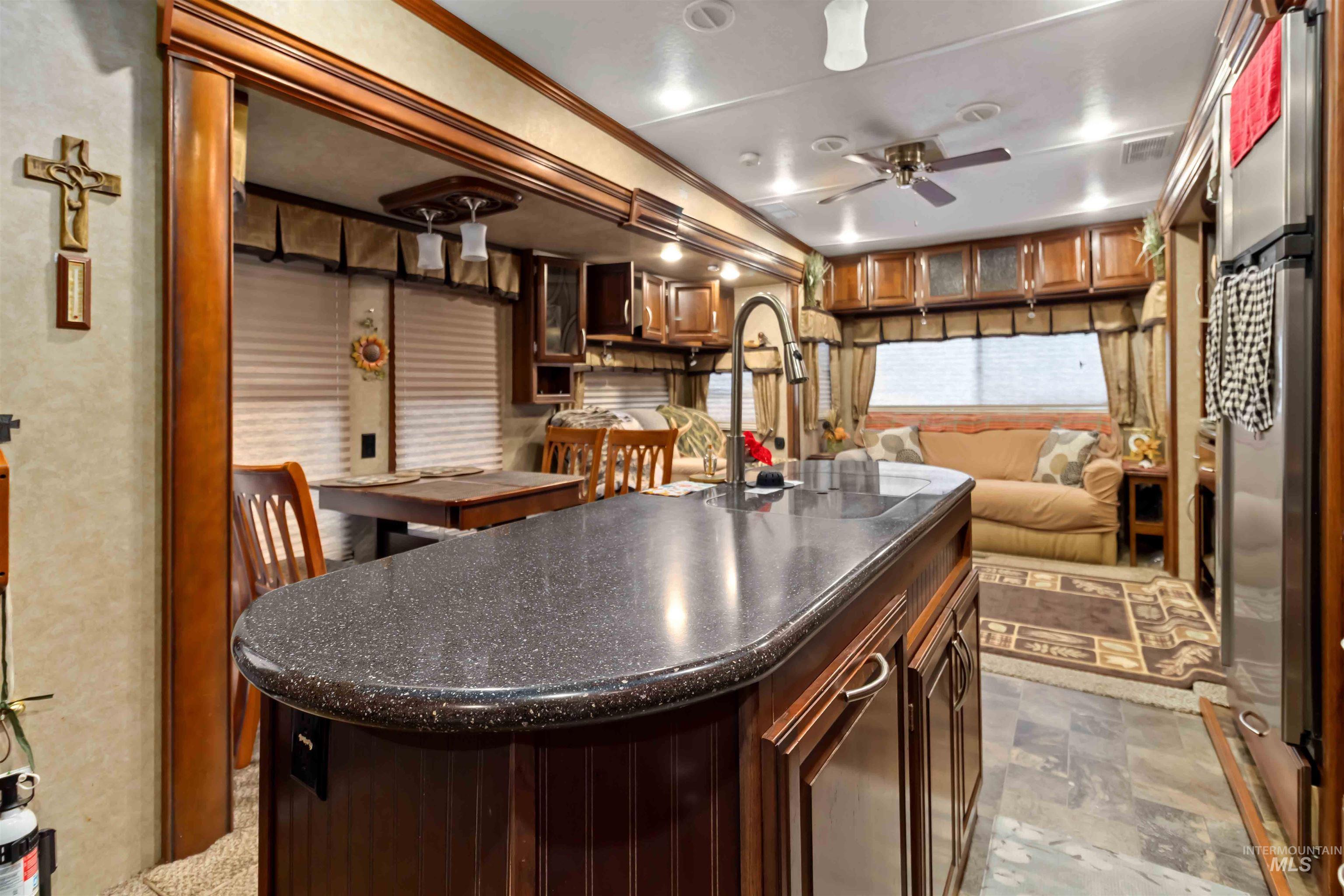 H05 North Sawyer Street Cascade, ID 83611 - Photo 9 of 40 Kitchen featuring dark brown cabinetry, a kitchen island with sink, glass insert cabinets, ceiling fan, and ornamental molding