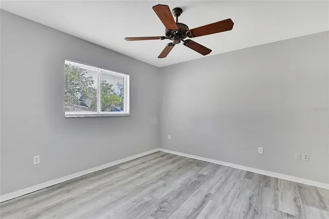 an empty room with wooden floor ceiling fan and windows