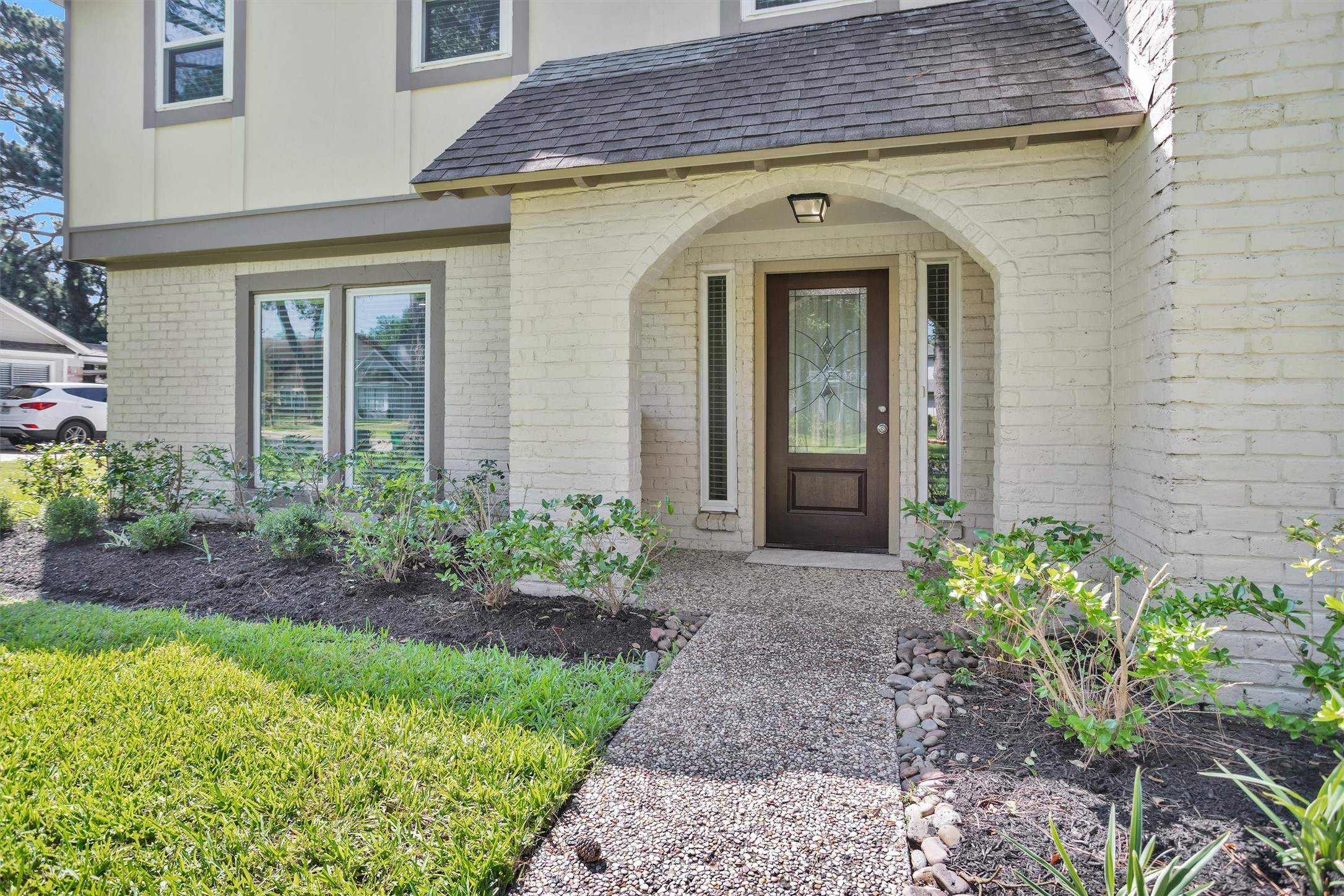9115 Godstone Lane Spring, TX 77379 - Photo 2 of 46 This photo showcases the inviting entrance of a home featuring a charming brick exterior with an arched doorway. The well-maintained front garden includes lush greenery and a neat pathway leading to the elegant front door with decorative glass panels.