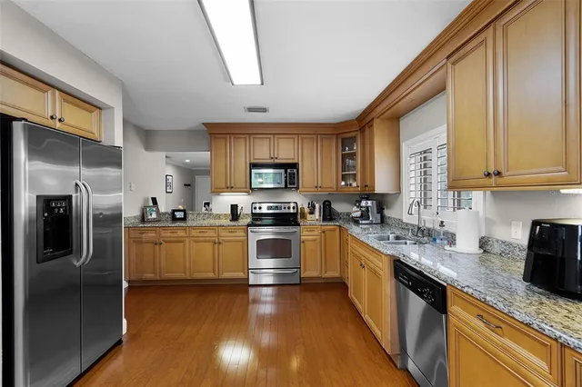 a kitchen with stainless steel appliances granite countertop a refrigerator a stove top oven a sink dishwasher and wooden cabinets with wooden floor
