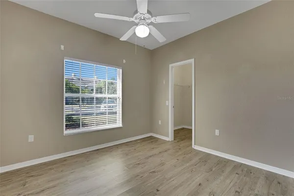 an empty room with wooden floor chandelier fan and windows