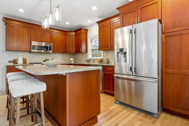 a kitchen with stainless steel appliances granite countertop a refrigerator a sink dishwasher a stove top oven a kitchen island and chairs with wooden floor