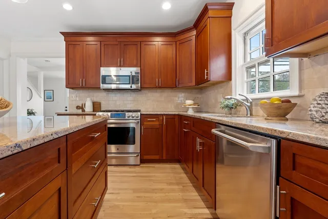 a kitchen with stainless steel appliances granite countertop wooden cabinets a sink and dishwasher next to a window