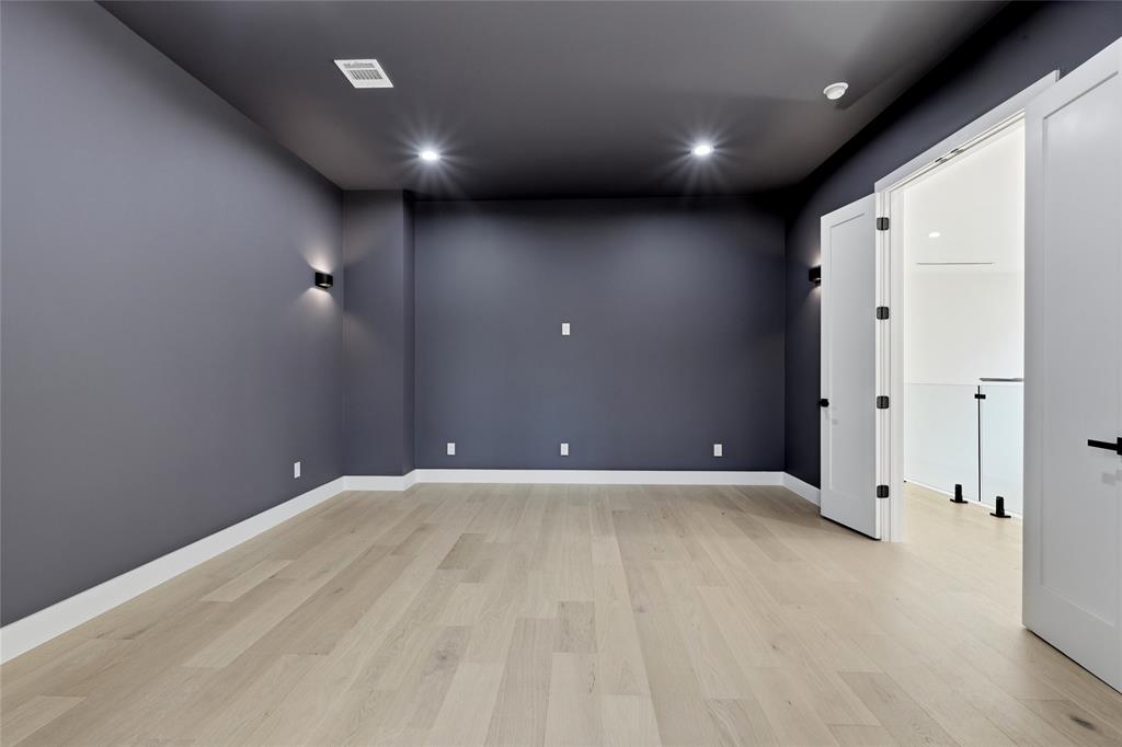 6038 Prospect Avenue Dallas, TX 75206 - Photo 31 of 40 Spacious room with light wood-finish flooring, dark accent walls, recessed lighting, wall sconces, and double doors opening to an adjacent area with a glass railing