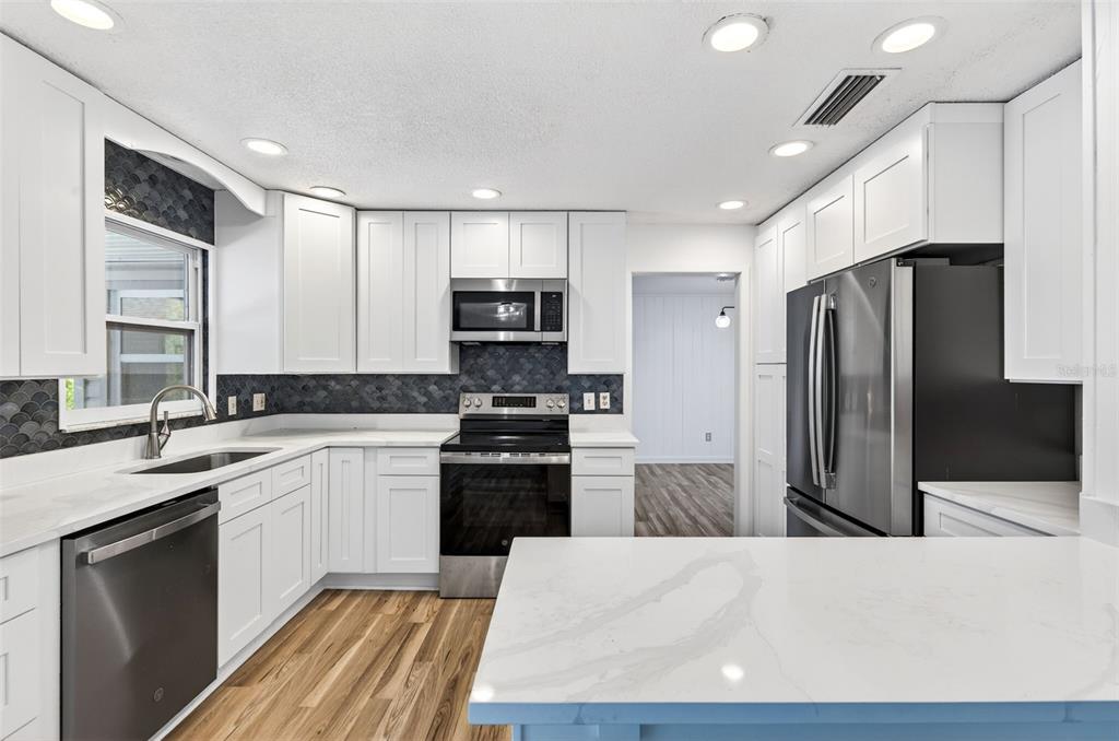 1520 South Keene Road Clearwater, FL 33756 - Photo 20 of 60 a large kitchen with a refrigerator a sink dishwasher a stove and white cabinets with wooden floor