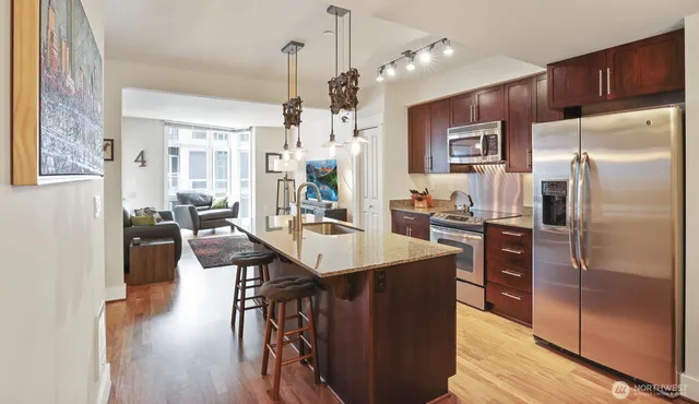 a kitchen with stainless steel appliances kitchen island granite countertop a refrigerator a sink dishwasher a dining table and chairs with wooden floor