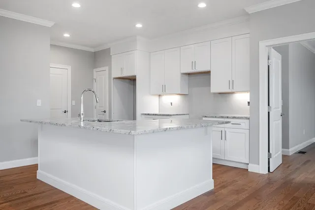 a kitchen with stainless steel appliances granite countertop a sink a stove a refrigerator and white cabinets with wooden floor