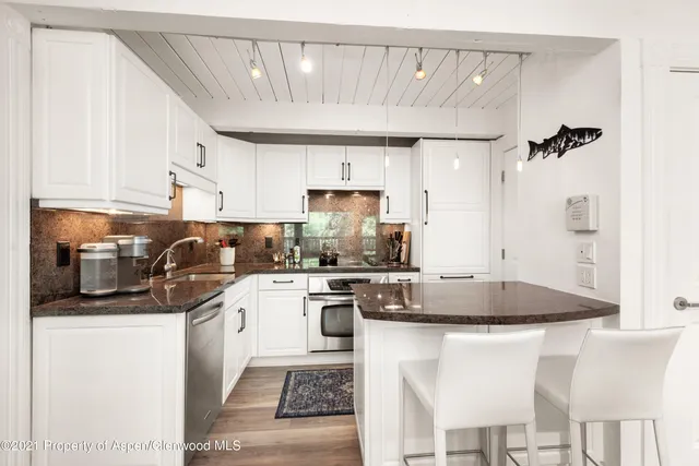 a kitchen with stainless steel appliances granite countertop a sink a stove a refrigerator cabinets and chairs