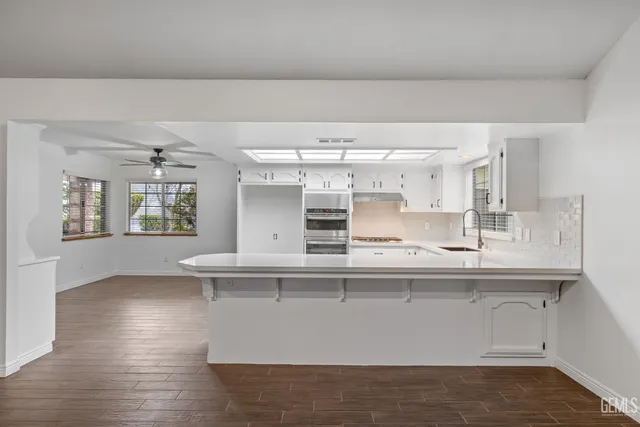 a kitchen with stainless steel appliances granite countertop a stove oven a sink dishwasher and white cabinets with wooden floor