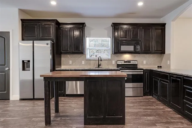 a kitchen with stainless steel appliances granite countertop a stove top oven a sink dishwasher a refrigerator and a dining table with wooden floor