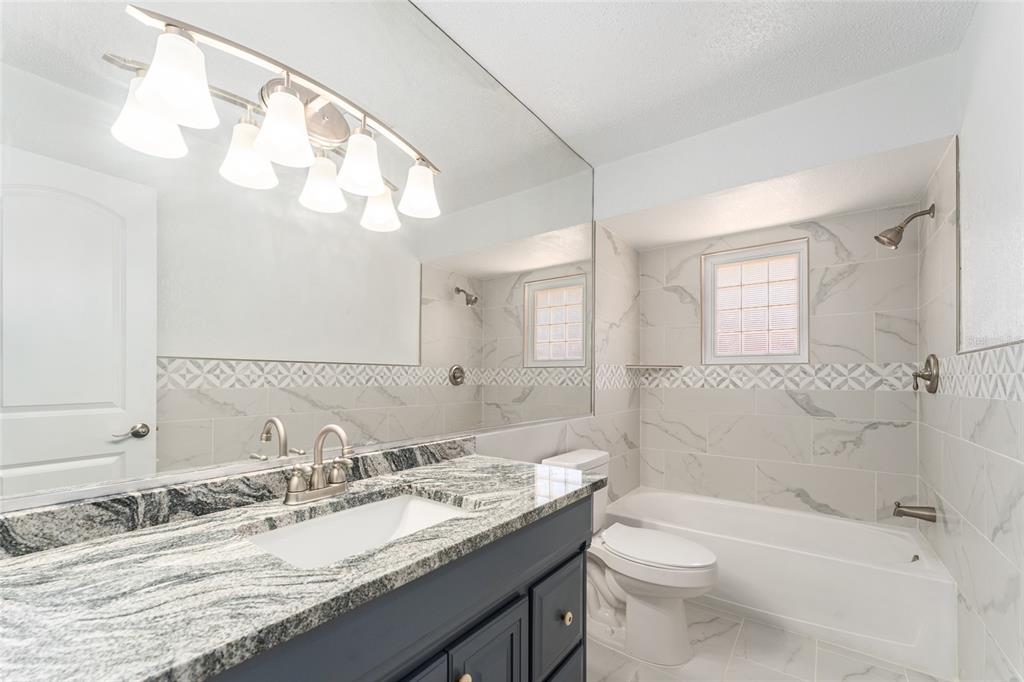 5041 Northeast 4th Street Ocala, FL 34470 - Photo 47 of 70 a bathroom with a granite countertop sink a toilet a mirror a bathtub and shower