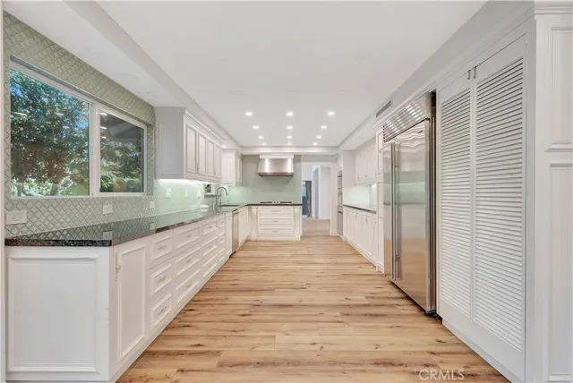 a large white kitchen with granite countertop lots of counter space wooden floor and stainless steel appliances