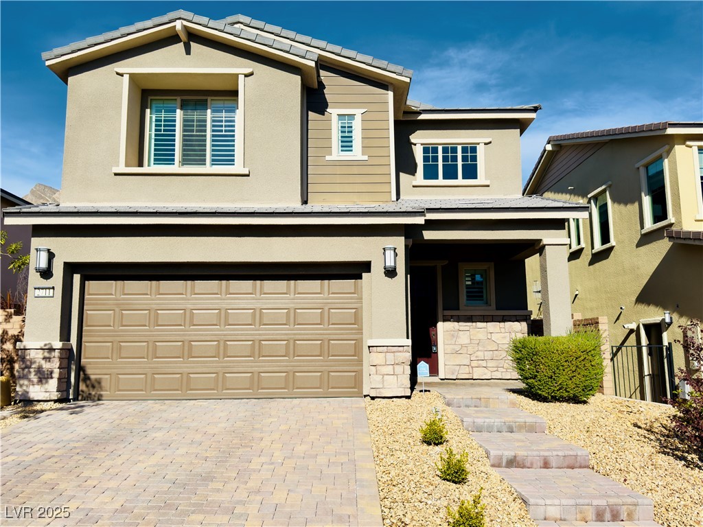 View of front facade with stone siding, stucco siding, decorative driveway, a garage, and covered porch
