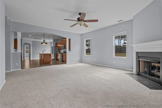 a view of a livingroom with a fireplace a ceiling fan and windows