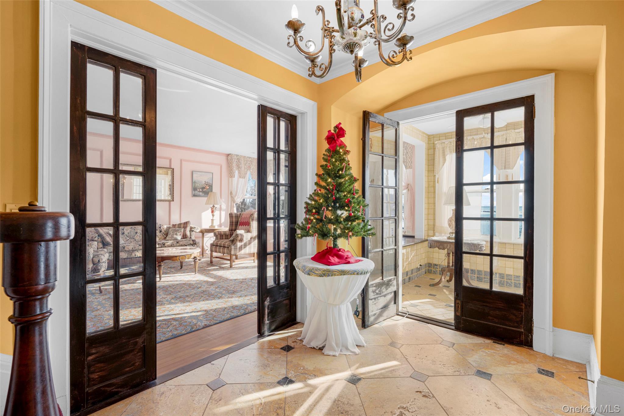 Foyer with french doors, a chandelier, healthy amount of natural light, crown molding, and stone tile floors