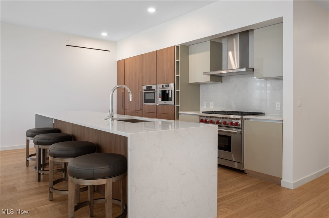 22700 Lake Road, Unit 204 Rocky River, OH 44116 - Photo 6 of 31 Kitchen with modern cabinets, tasteful backsplash, a kitchen breakfast bar, appliances with stainless steel finishes, and wall chimney range hood