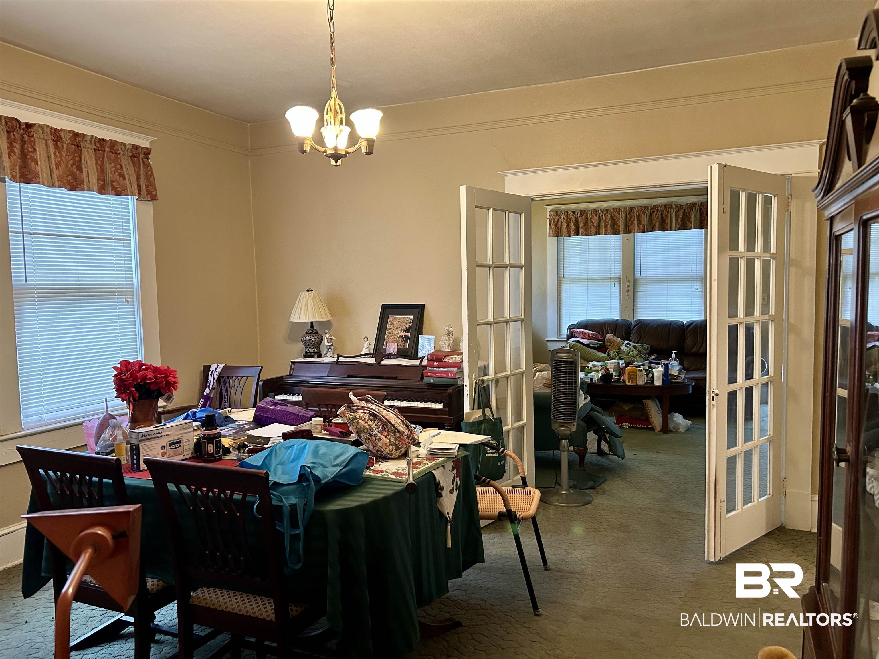 302 Stocking Street Mobile, AL 36604 - Photo 31 of 31 Dining area featuring a classic three-light chandelier, a large window with horizontal blinds, and paneled French doors leading to an additional space