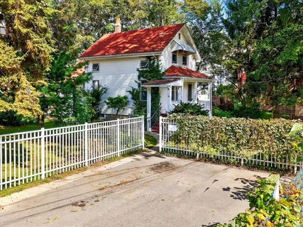 a view of a white house with large trees and wooden fence