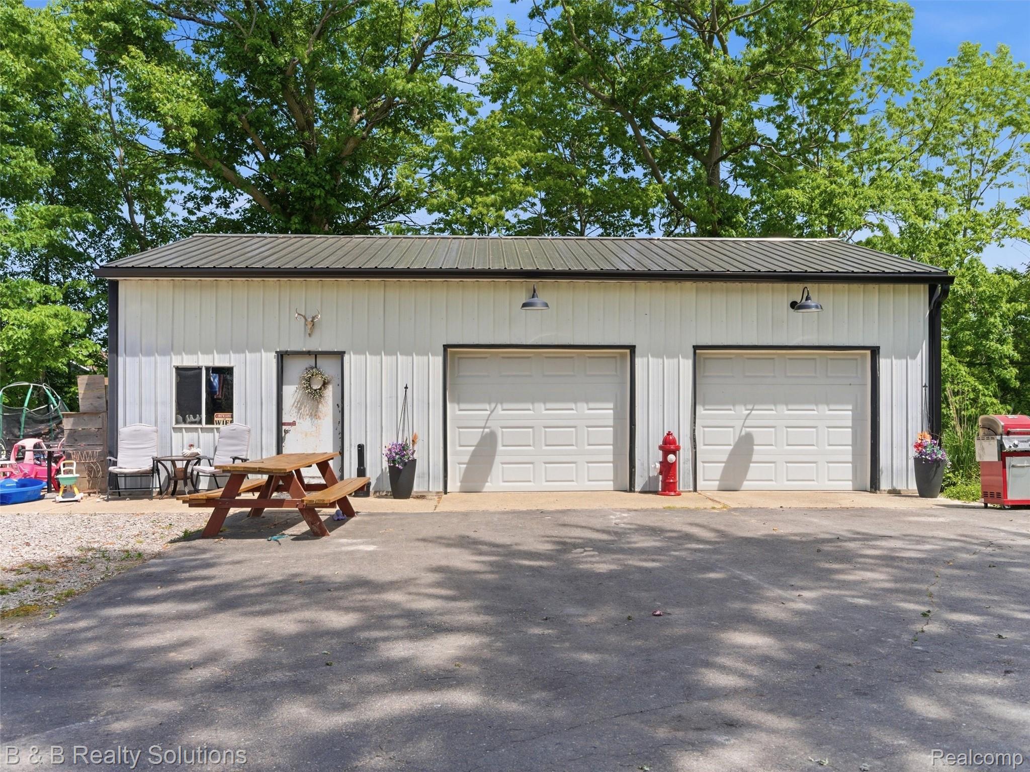 60455 Bates Road New Haven, MI 48048 - Photo 26 of 58 White metal-sided outbuilding with a black metal roof, featuring two garage doors, an entry door, and a single window