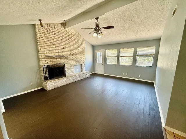 an empty room with wooden floor fireplace and windows