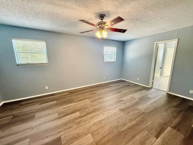 an empty room with wooden floor fan and windows