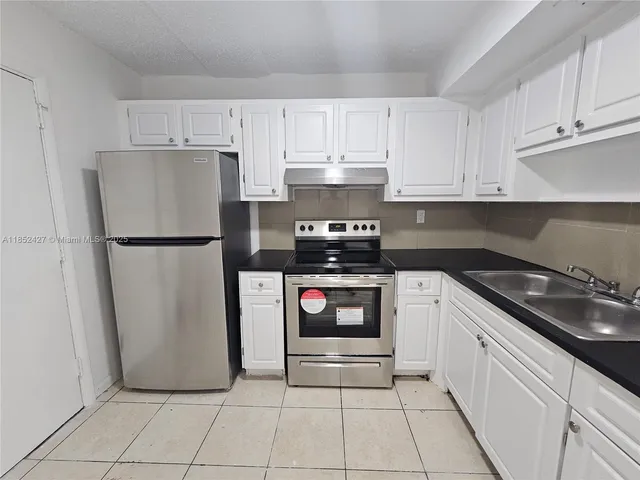 a kitchen with granite countertop white cabinets and refrigerator
