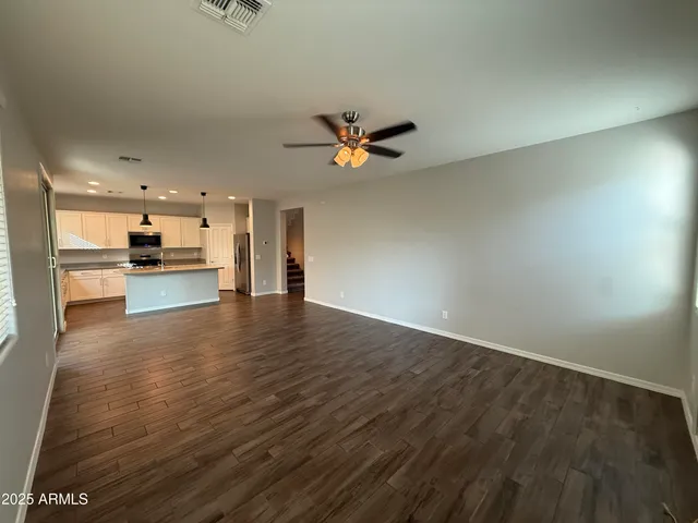 a view of an empty room with chandelier fan and wooden floor