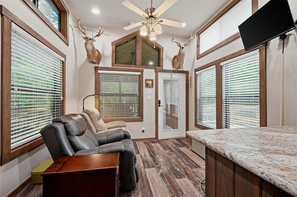 3958 Ranch Road Whitesboro, TX 76273 - Photo 11 of 40 Living room with a ceiling fan, wood-finish flooring, multiple windows with blinds, wood trim detailing, and a stone-look countertop on a built-in bar