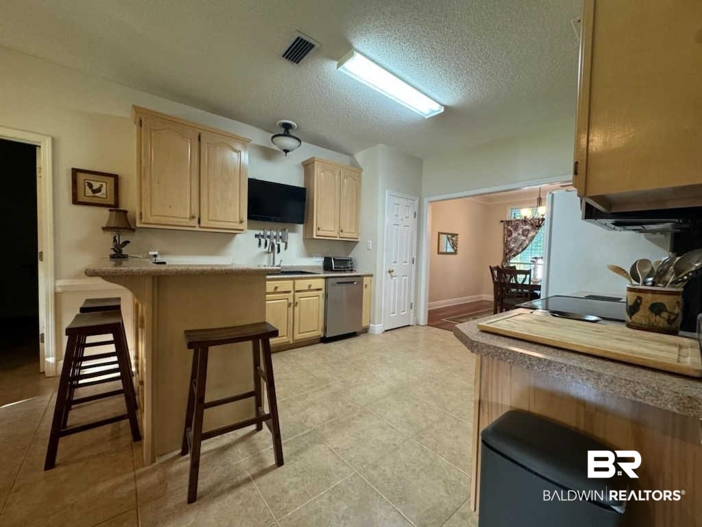 31163 Woodland Way Daphne, AL 36527 - Photo 18 of 44 Kitchen with a chandelier, stainless steel dishwasher, light brown cabinets, light tile patterned floors, and a breakfast bar