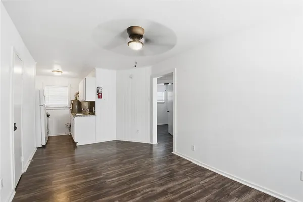a view of an empty room with wooden floor and a kitchen