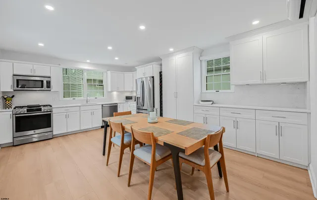 a kitchen with stainless steel appliances granite countertop a stove a sink a microwave a refrigerator white cabinets and wooden floor