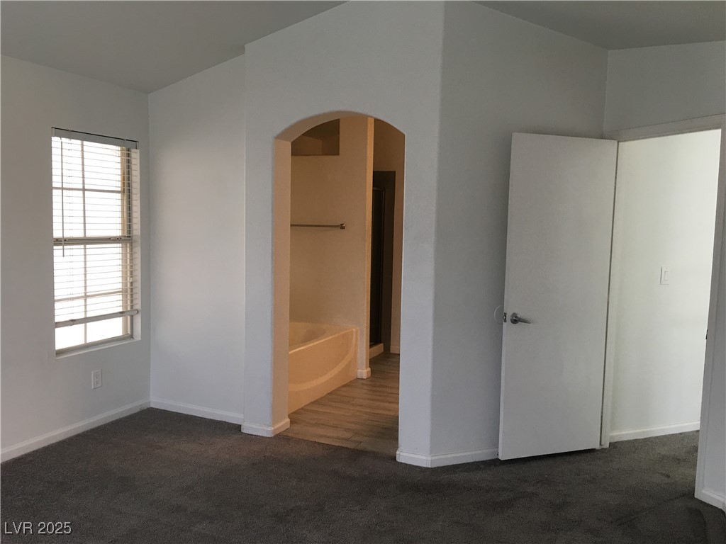 973 Cedar Pines Street Henderson, NV 89011 - Photo 20 of 37 Unfurnished bedroom featuring arched walkways, dark colored carpet, and ensuite bath