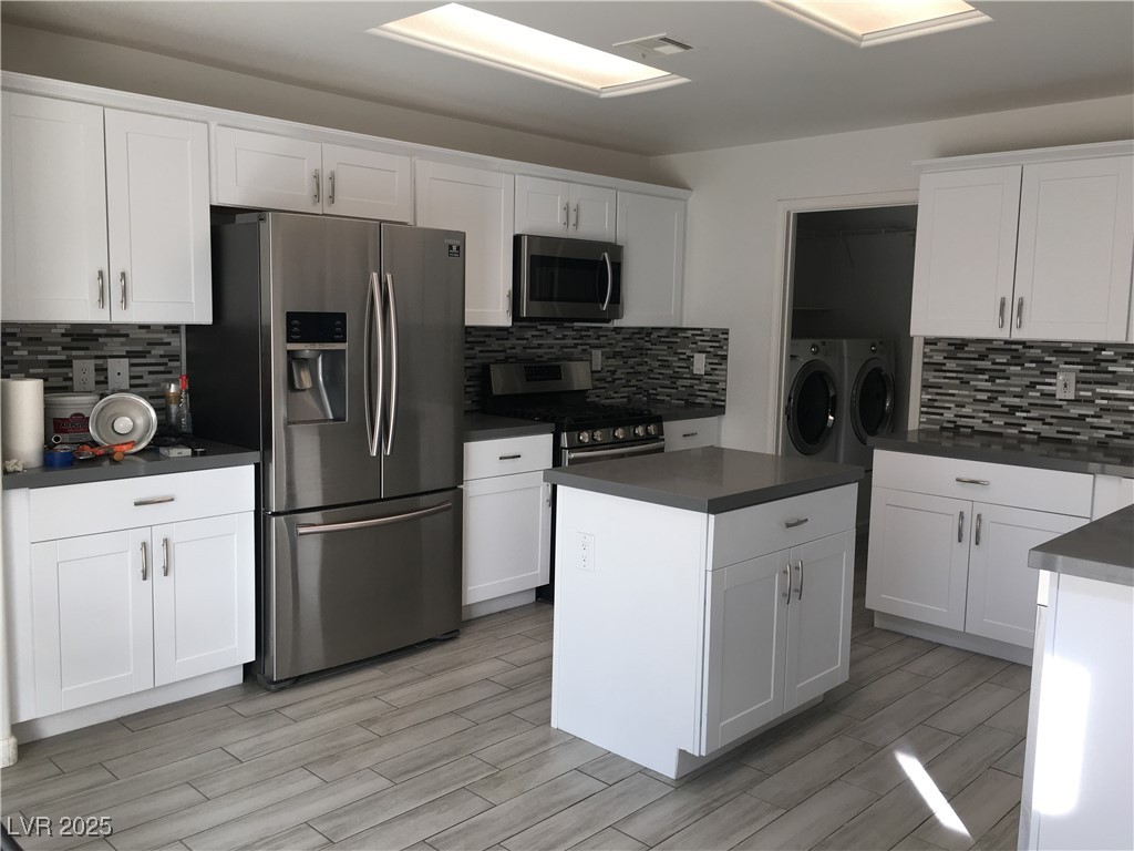 973 Cedar Pines Street Henderson, NV 89011 - Photo 9 of 37 Kitchen featuring dark countertops, stainless steel appliances, backsplash, independent washer and dryer, and white cabinets