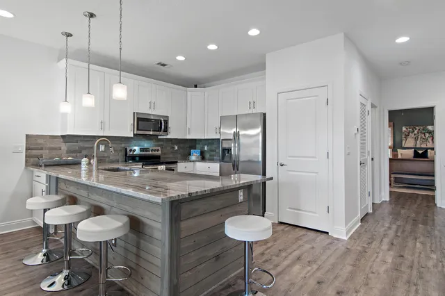 a kitchen with stainless steel appliances granite countertop a stove a refrigerator a kitchen island a sink cabinets and wooden floor