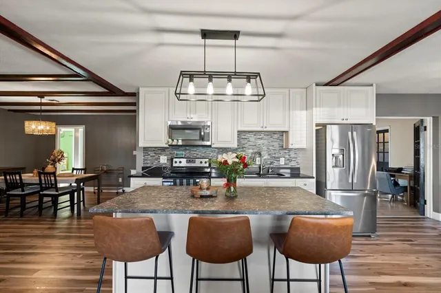 a kitchen with stainless steel appliances granite countertop a dining table chairs refrigerator and cabinets