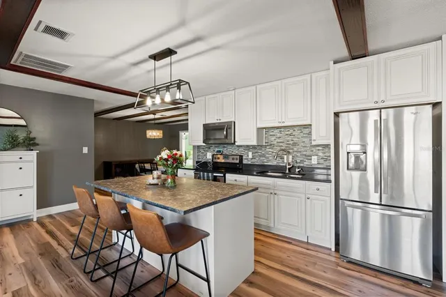 a kitchen with stainless steel appliances granite countertop a dining table chairs refrigerator and microwave