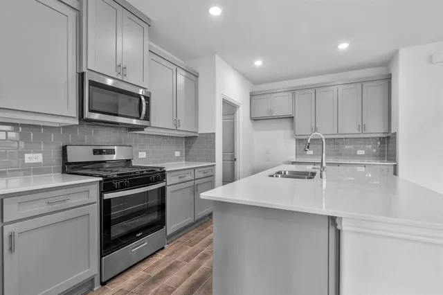 a kitchen with stainless steel appliances a sink dishwasher a stove top oven a refrigerator with grey cabinets and wooden floor