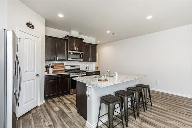 a kitchen with stainless steel appliances granite countertop a stove a refrigerator a sink a dining table and chairs