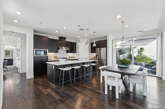 a kitchen with kitchen island a dining table chairs wooden floor and appliances