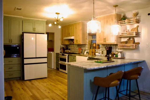 a kitchen with stainless steel appliances a refrigerator a sink dishwasher a stove and white cabinets with wooden floor