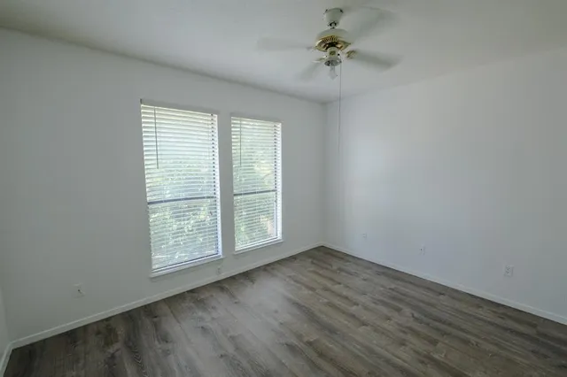 an empty room with wooden floor chandelier fan and windows