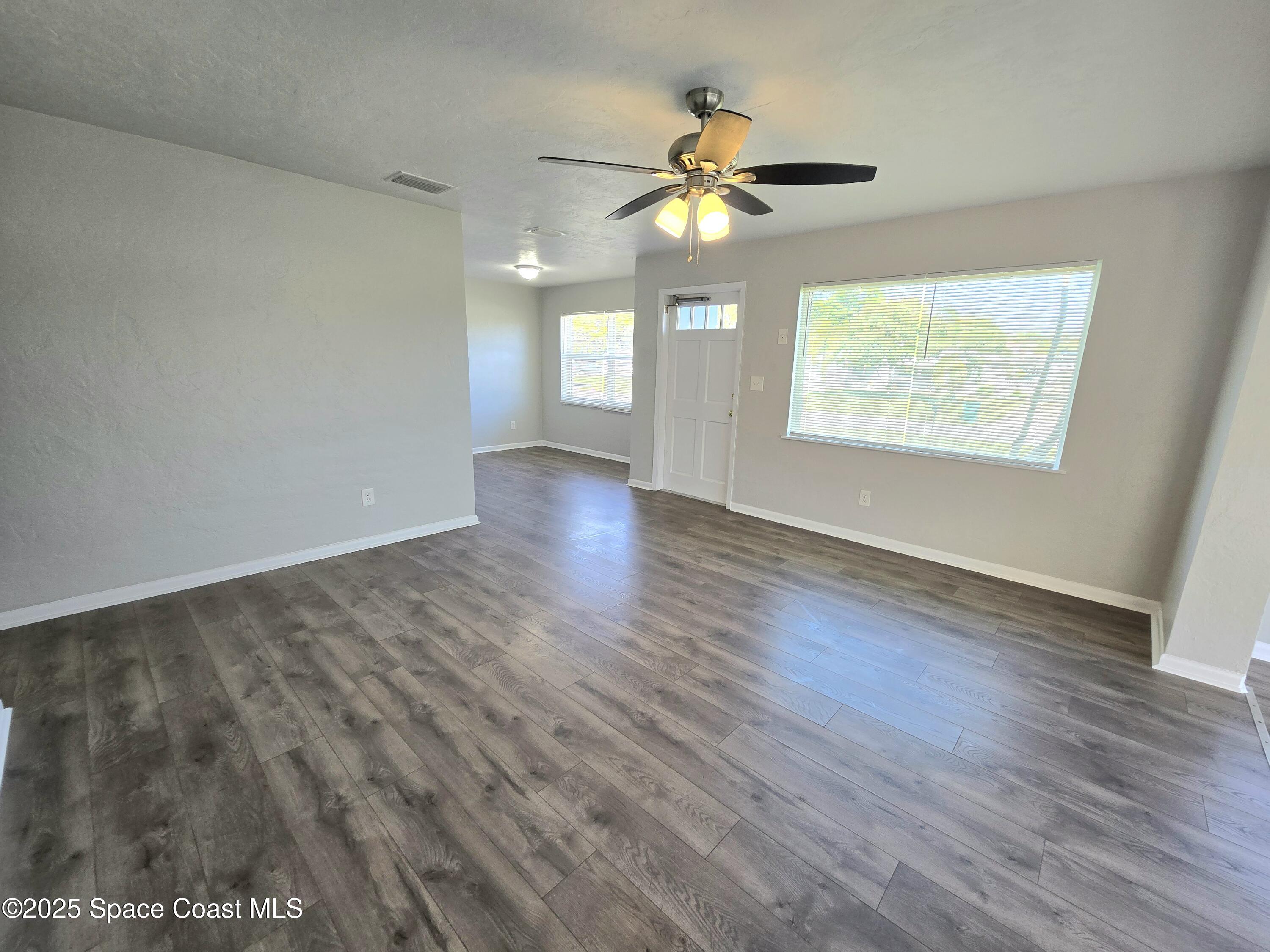 2373 Allan Adale Road Melbourne, FL 32935 - Photo 3 of 19 an empty room with wooden floor chandelier fan and windows