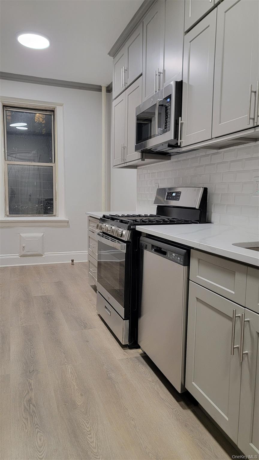 34-58 90th Street, Unit R5 Queens, NY 11372 - Photo 10 of 14 Kitchen with stainless steel appliances, light wood-type flooring, tasteful backsplash, light stone counters, and recessed lighting