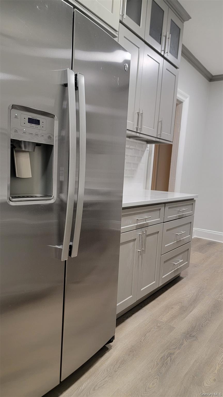 34-58 90th Street, Unit R5 Queens, NY 11372 - Photo 6 of 14 Kitchen with stainless steel refrigerator with ice dispenser, light wood-style floors, ornamental molding, gray cabinetry, and glass insert cabinets