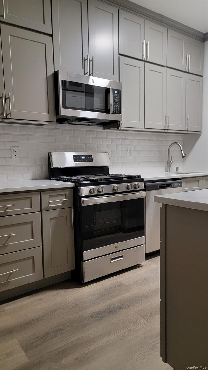 34-58 90th Street, Unit R5 Queens, NY 11372 - Photo 7 of 14 Kitchen featuring gray cabinets, stainless steel appliances, light wood-style flooring, and backsplash