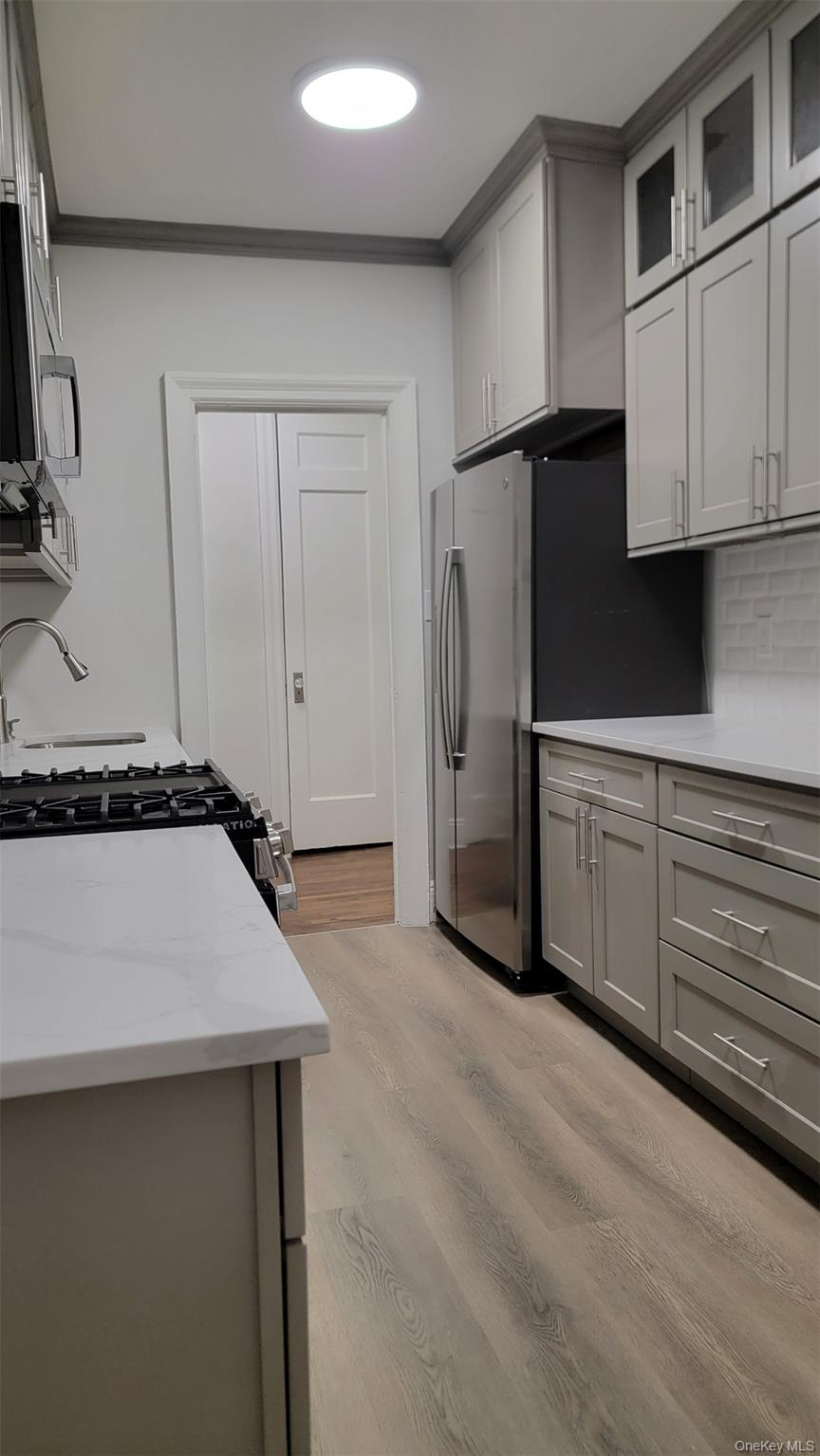 34-58 90th Street, Unit R5 Queens, NY 11372 - Photo 8 of 14 Kitchen featuring light wood-type flooring, gray cabinets, light stone counters, appliances with stainless steel finishes, and glass insert cabinets