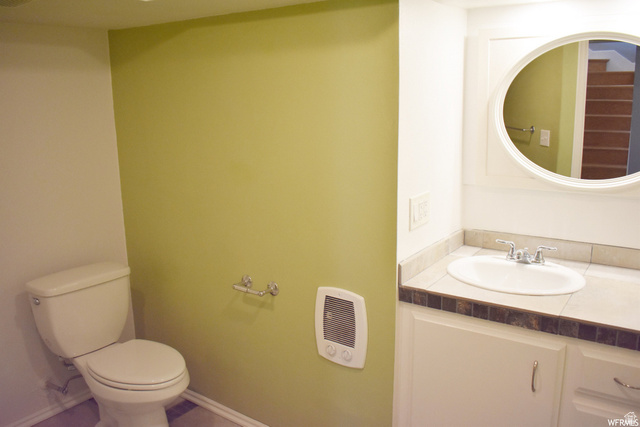 490 Averett Avenue Springville, UT 84663 - Photo 8 of 14 Bathroom featuring a white toilet, light green accent wall, white vanity with integrated sink, stone-look countertop, and an oval mirror